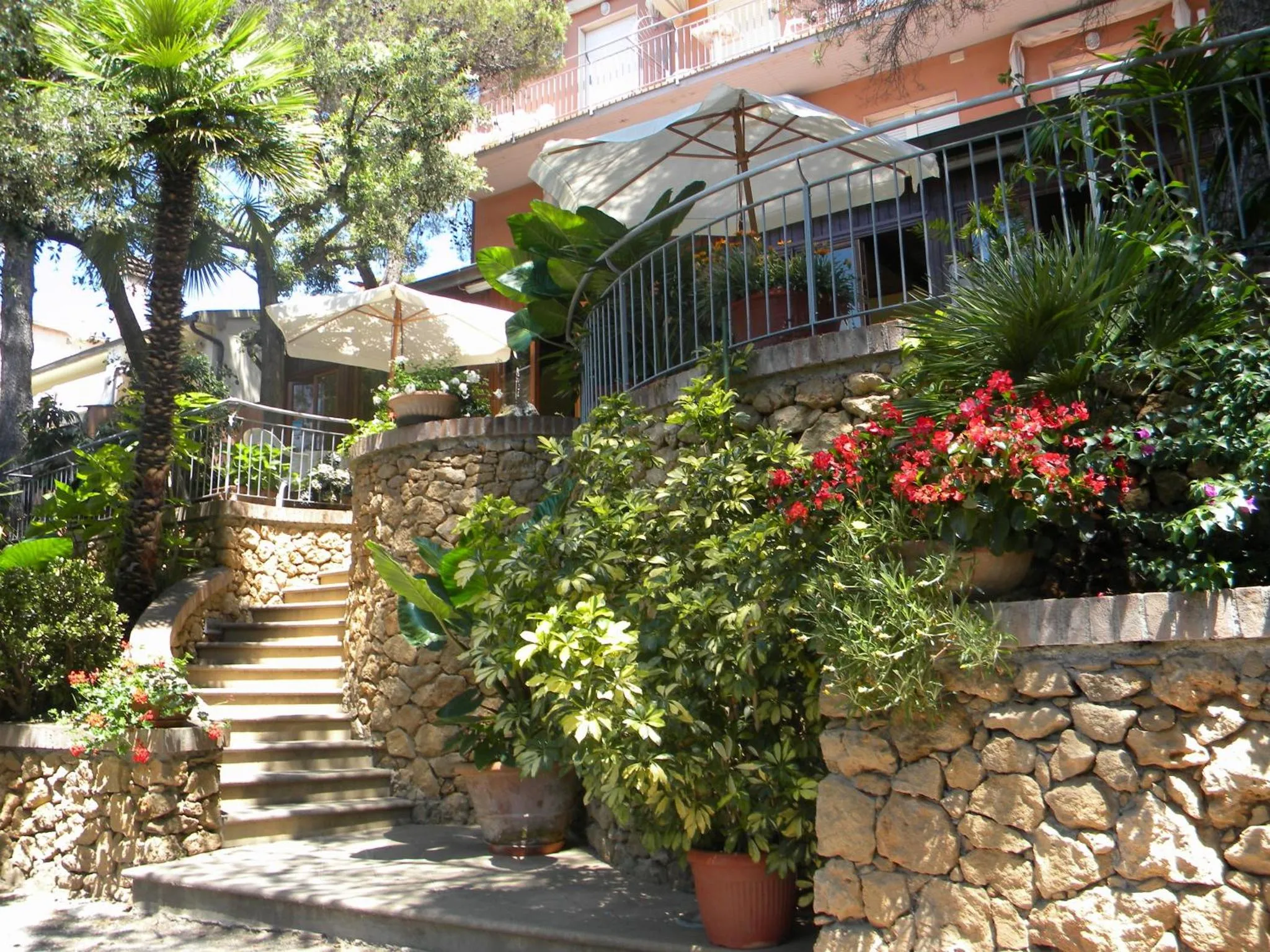 Jardin fleuri avec escalier en pierre menant à une terrasse ombragée.