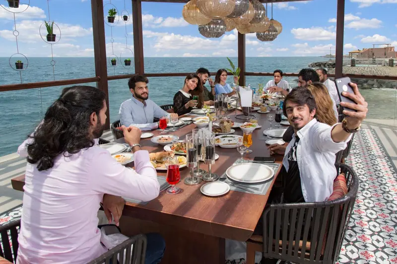 Une table de convives partage un repas dans une salle à manger ouverte sur la mer.