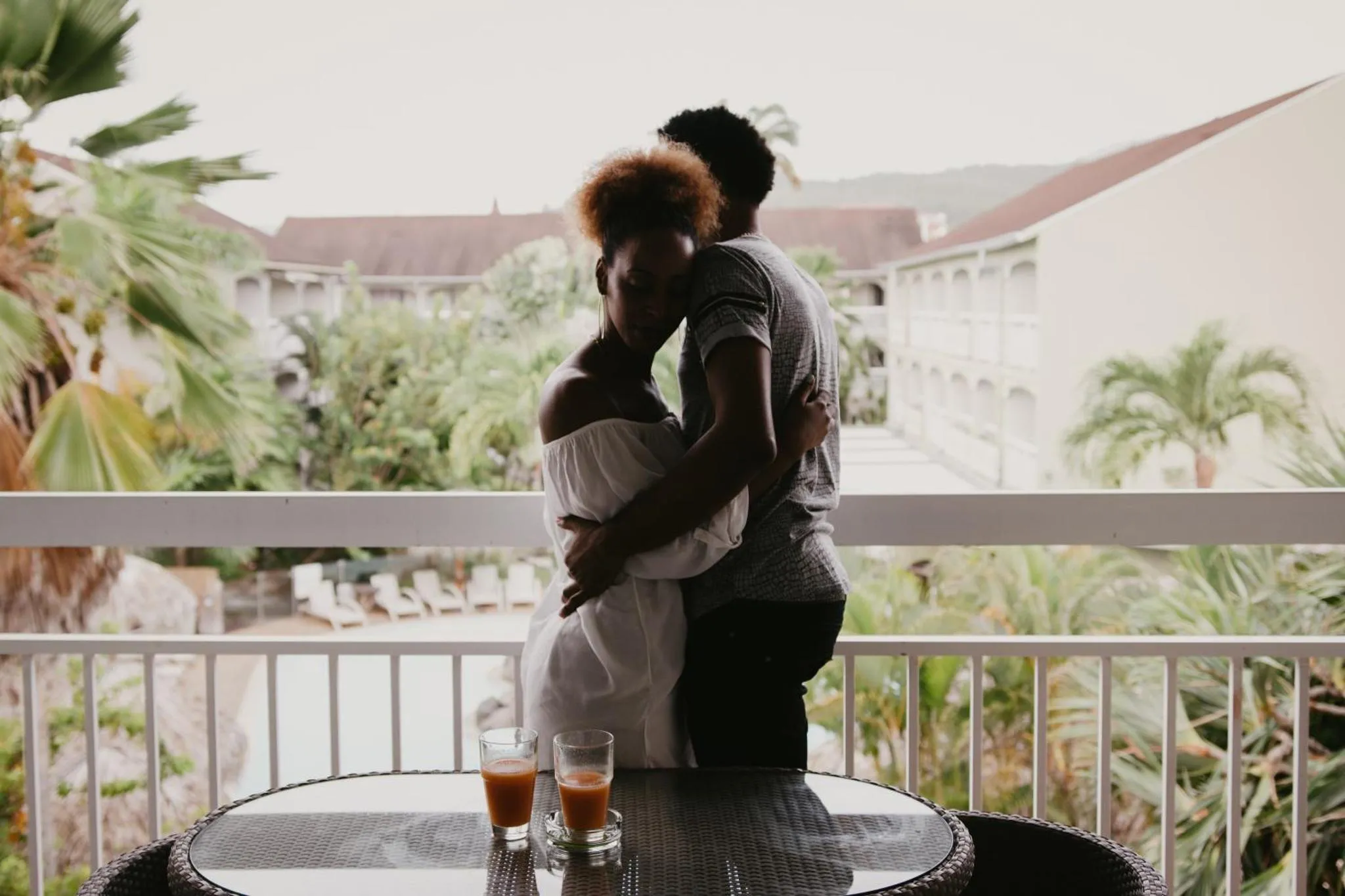 Un couple s'embrasse sur une terrasse avec vue sur la végétation et des bâtiments.