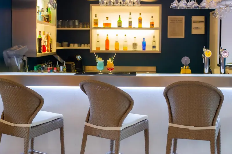 Un comptoir de bar moderne avec des tabourets et des bouteilles colorées.