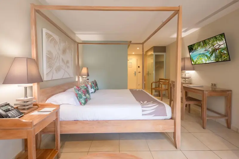 Une chambre lumineuse avec un grand lit à baldaquin et une télévision murale.