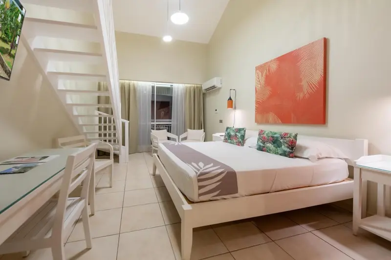 Une chambre lumineuse avec un lit double et un escalier menant à une mezzanine.
