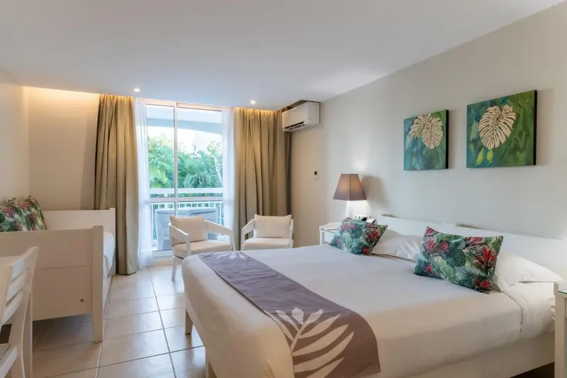 Une chambre lumineuse avec un lit double et un coin salon donnant sur une terrasse.