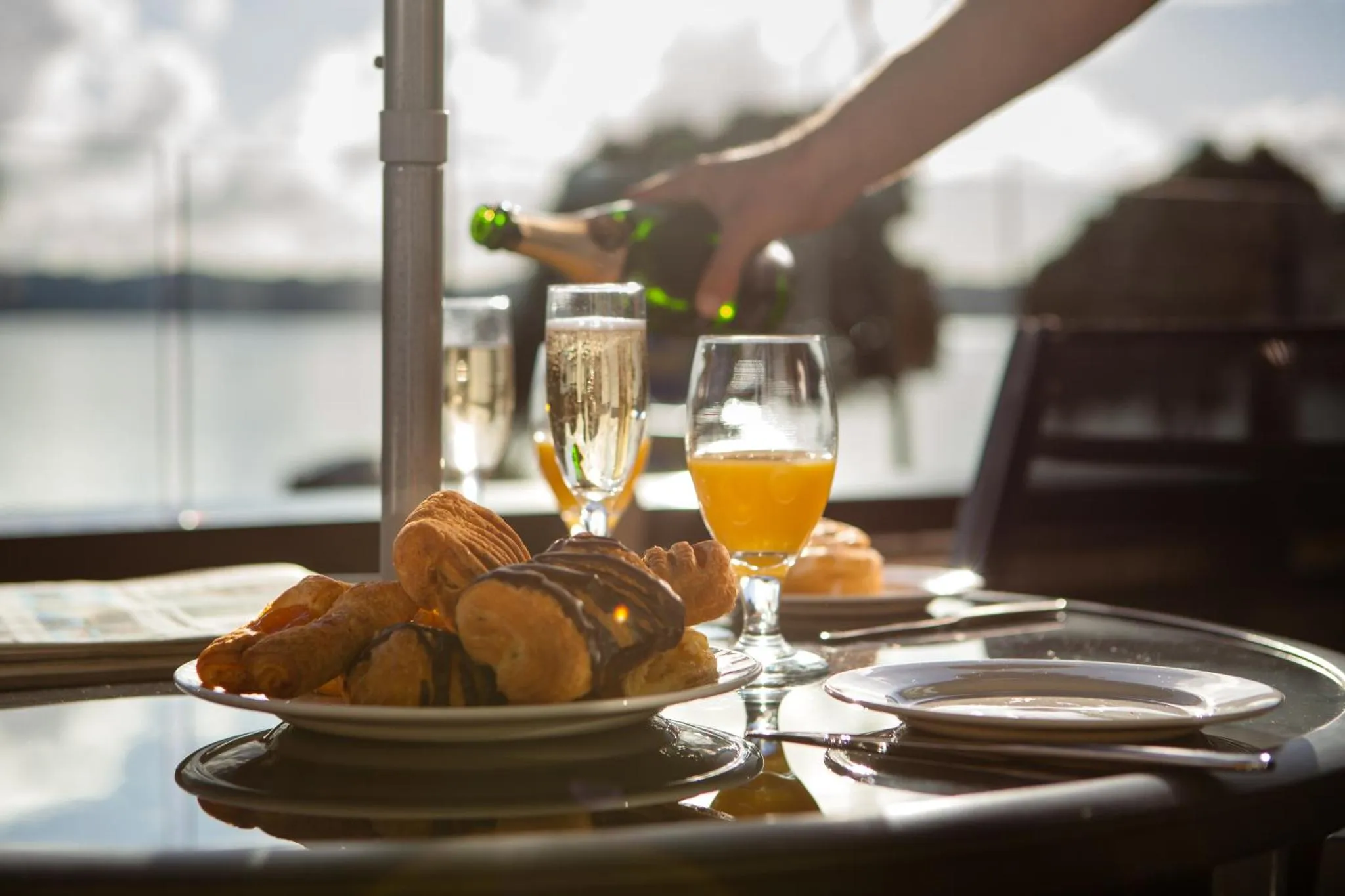 Une table est dressée avec des viennoiseries et des boissons, face à la mer.