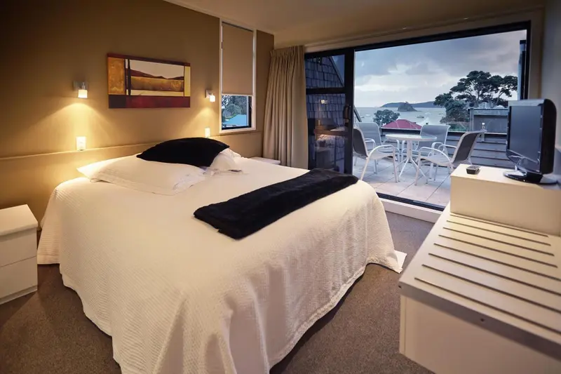Chambre lumineuse avec un grand lit et une vue sur la mer par une baie vitrée.
