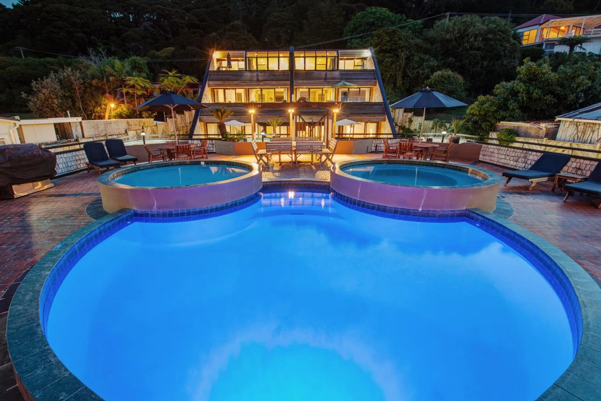 Une piscine illuminée devant un bâtiment avec des terrasses et des transats.