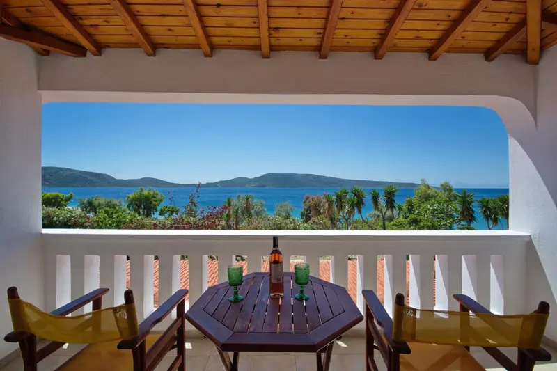 Une table et des chaises en bois sont disposées sur une terrasse avec vue sur la mer.