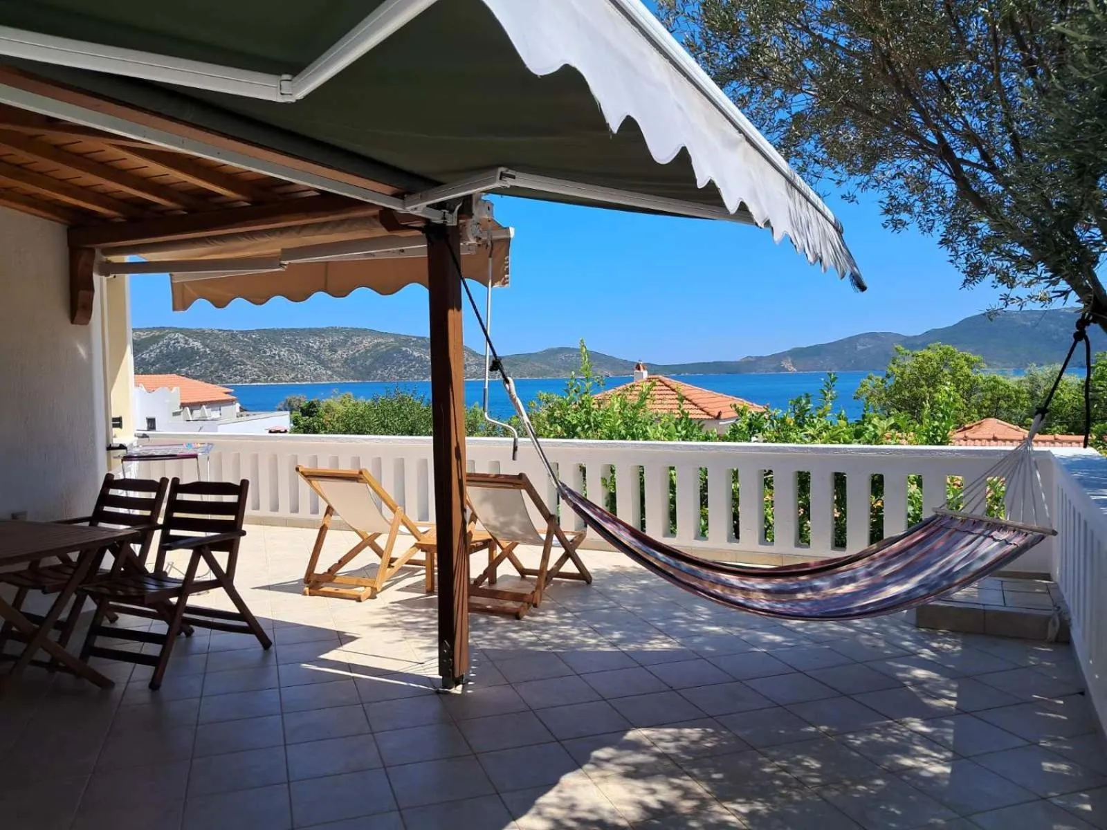 Terrasse carrelée avec mobilier de jardin et hamac face à la mer.