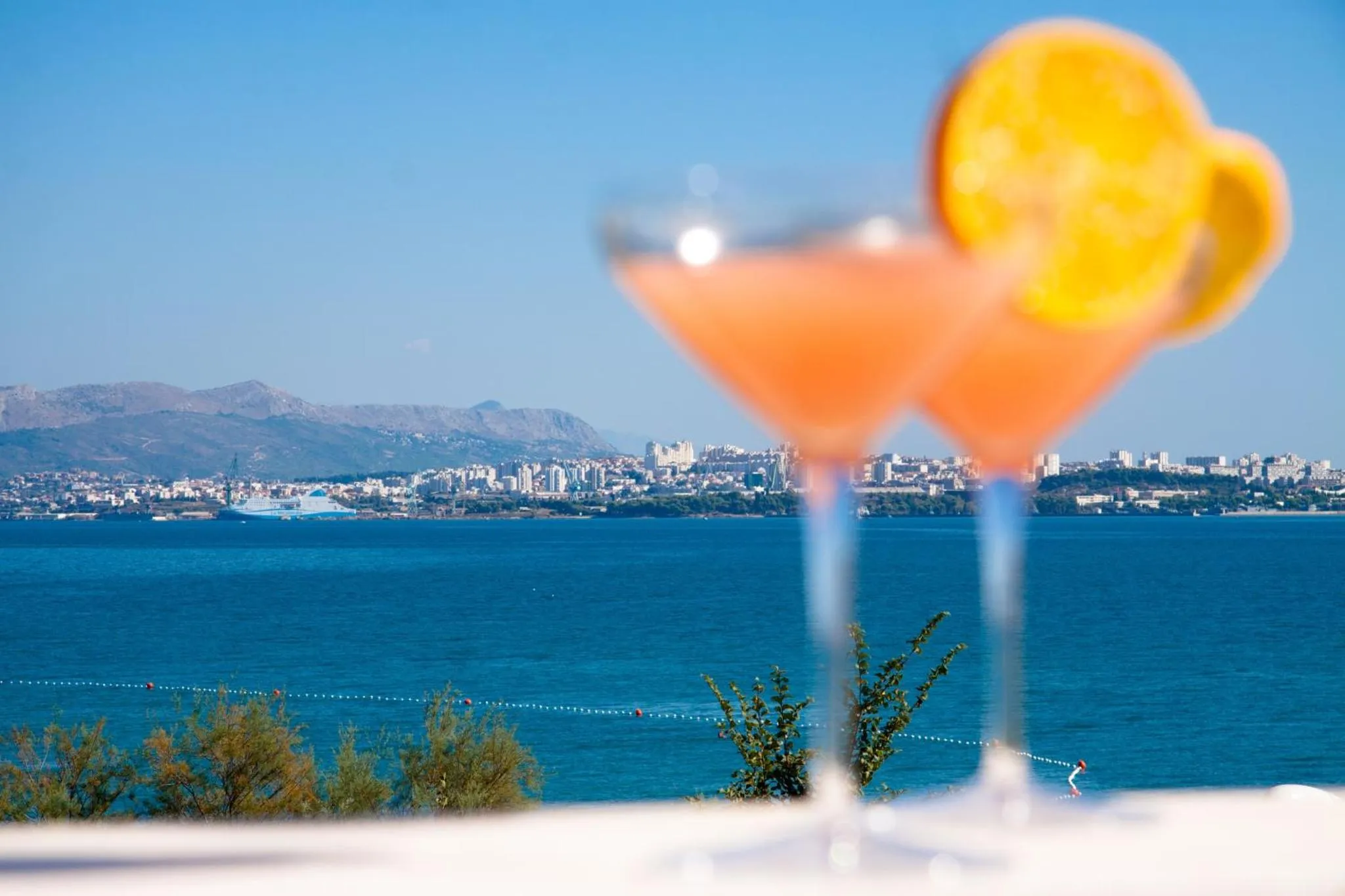 Deux cocktails colorés sur une terrasse avec vue sur la mer et la ville.