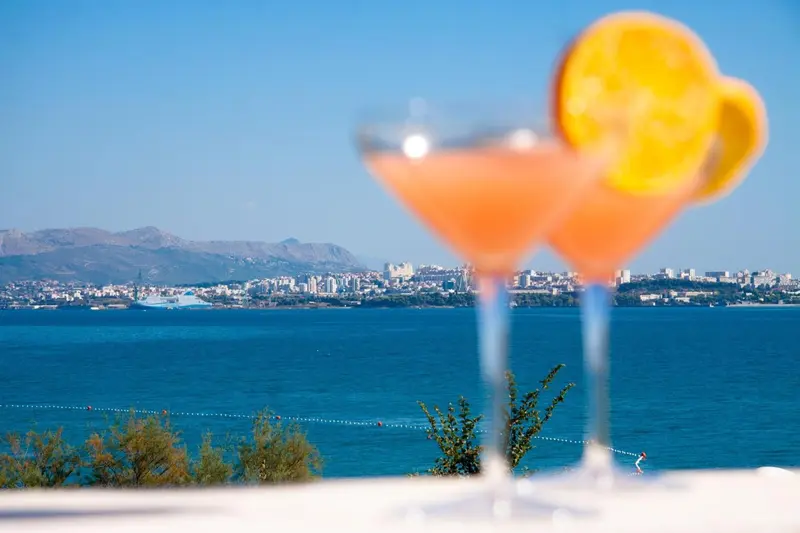 Deux cocktails colorés sur une terrasse avec vue sur la mer et la ville.