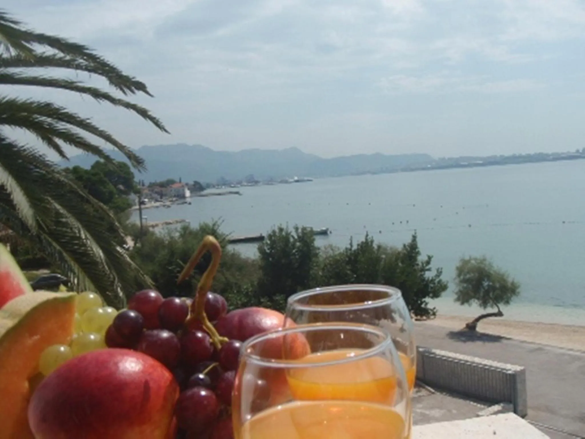 Deux verres de jus de fruits et des fruits frais sur une table avec vue sur la mer et les montagnes.