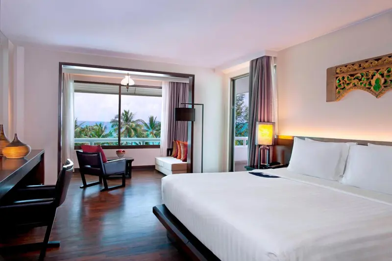 Chambre lumineuse avec un lit et un espace détente donnant sur une vue tropicale.