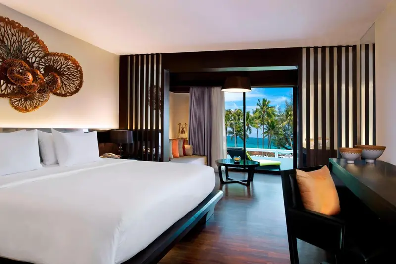 Une chambre lumineuse avec un grand lit et un espace salon donnant sur une vue tropicale.