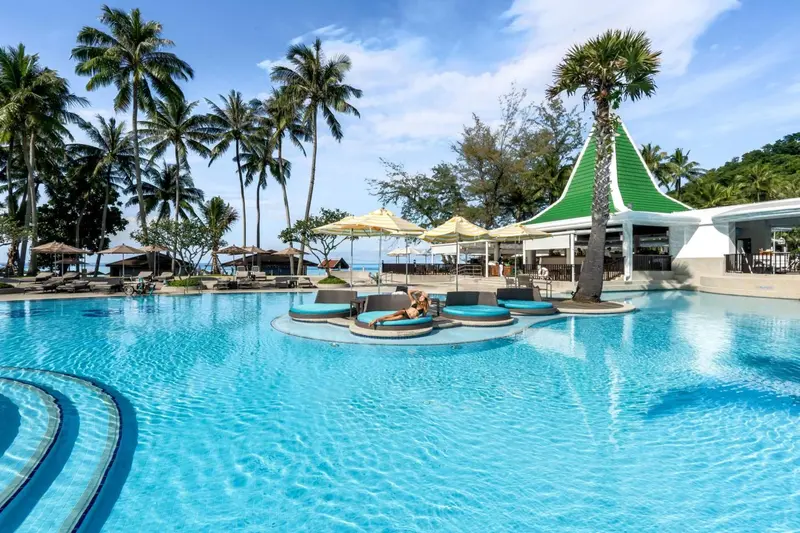 Une piscine turquoise bordée de transats et de palmiers.