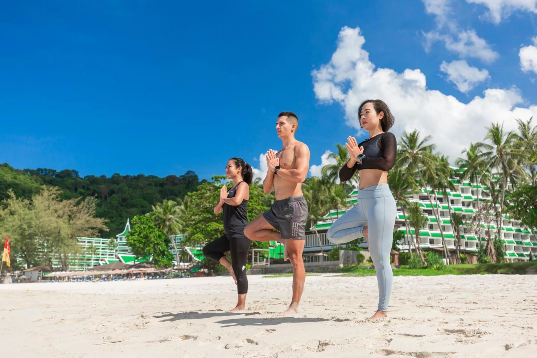 Des personnes pratiquent le yoga sur une plage de sable blanc face à la mer.