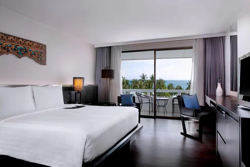 Une chambre lumineuse avec un grand lit et un accès à un balcon donnant sur la mer.