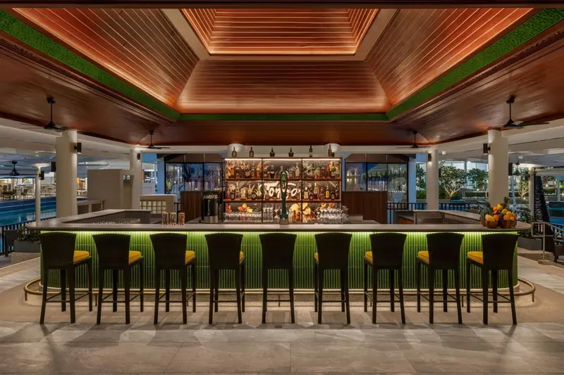 Un long comptoir de bar moderne avec des tabourets verts et des bouteilles illuminées.