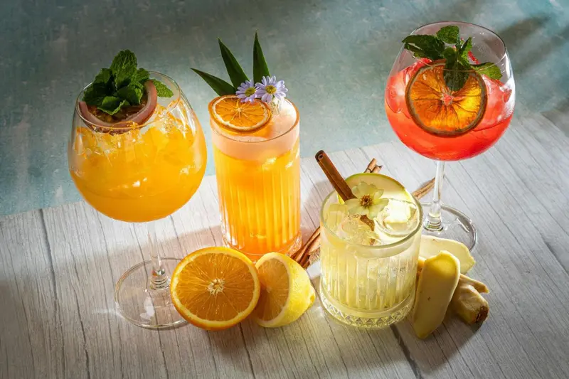 Trois cocktails colorés et des fruits frais disposés sur une table en bois.