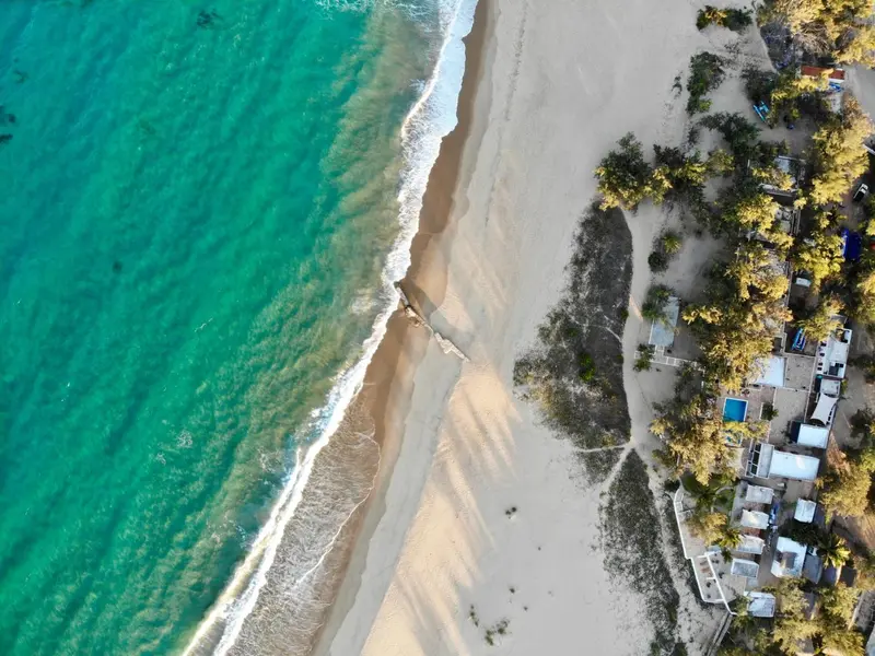 Vue aérienne d'une plage de sable fin bordée d'une eau turquoise et d'une végétation luxuriante.