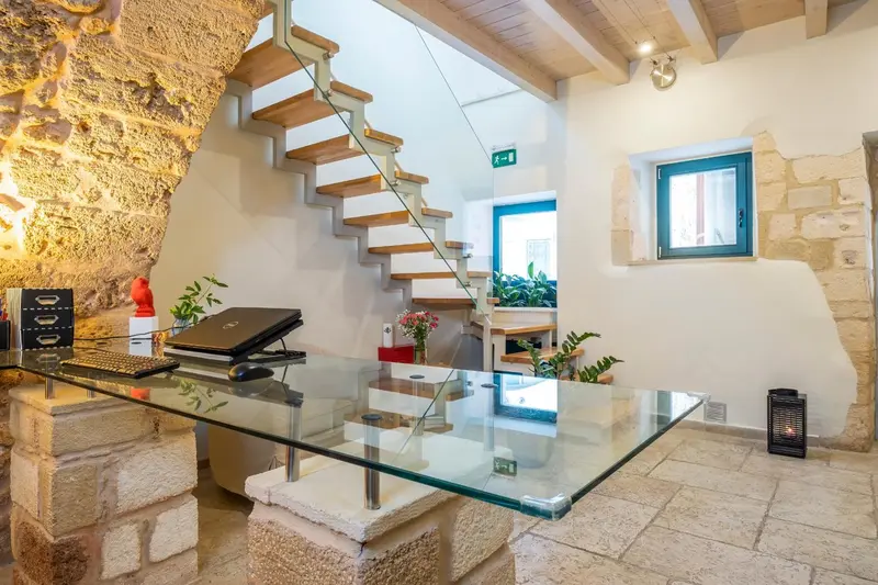 Un comptoir d'accueil en verre est devant un mur en pierre et un escalier en bois.