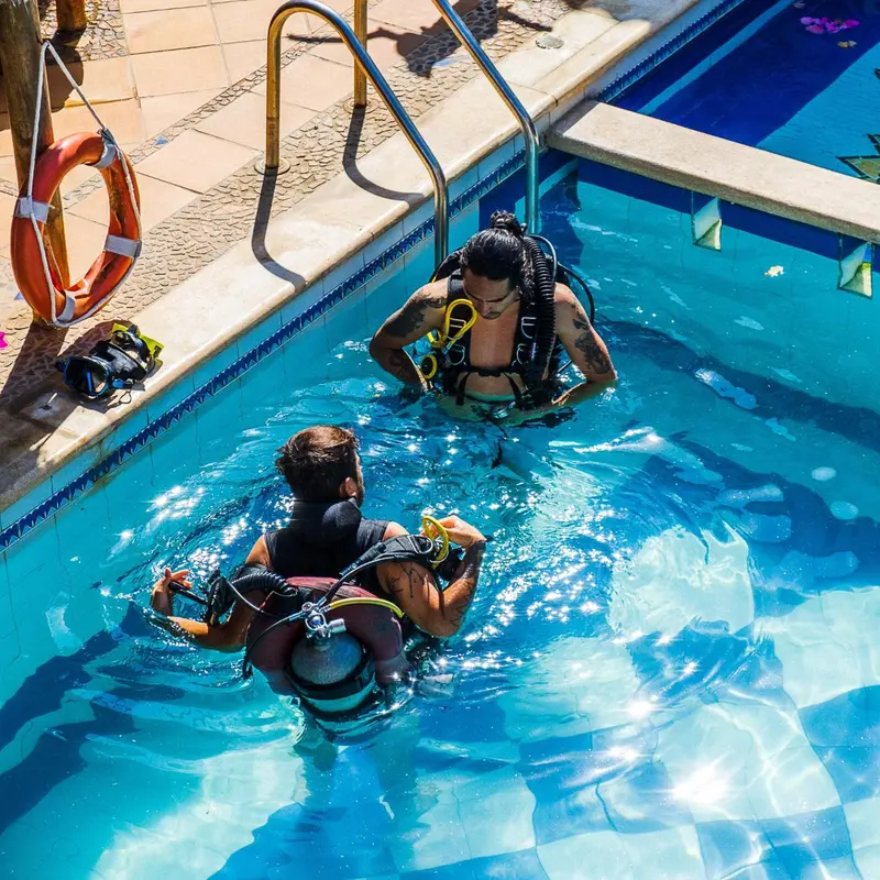 Deux personnes équipées de matériel de plongée s'immergent dans une piscine.