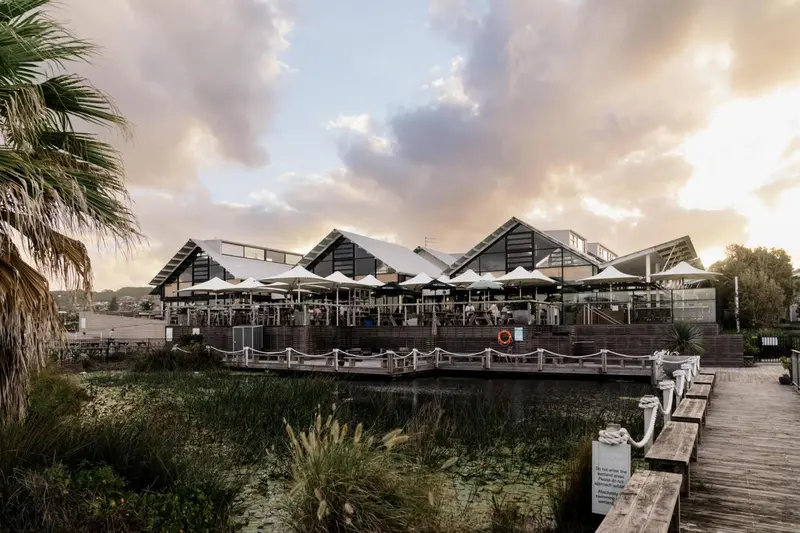 Terrasse de restaurant avec vue sur un plan d'eau au coucher du soleil.