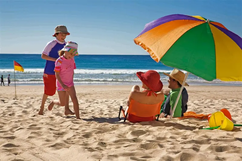 Des enfants jouent sur une plage ensoleillée sous un parasol coloré.
