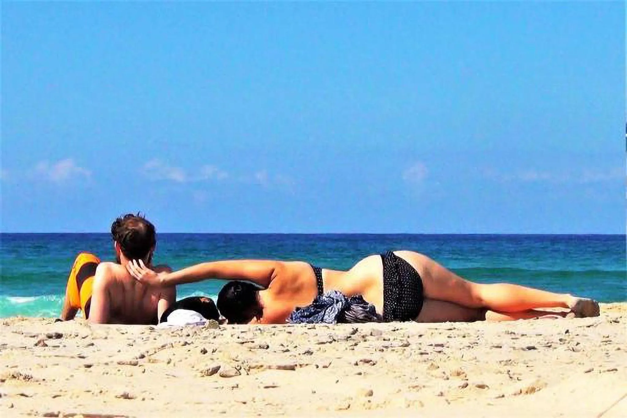 Couple se relaxant sur une plage de sable fin face à la mer.