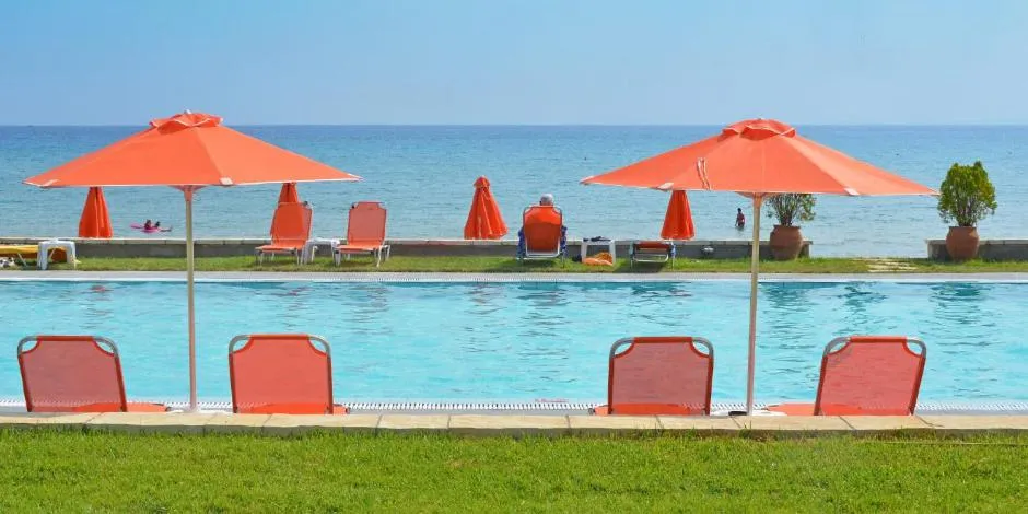 Transats oranges disposés devant une piscine turquoise en bord de mer.