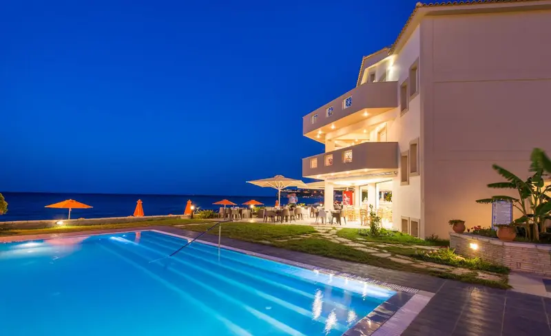 Bâtiment blanc éclairé au crépuscule avec piscine au premier plan et mobilier de jardin.