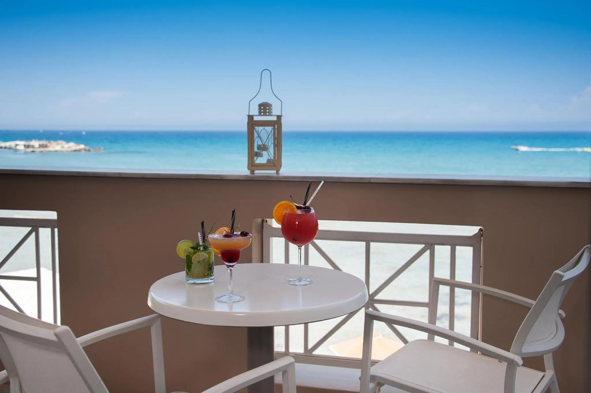Deux cocktails colorés sur une table ronde sur une terrasse ensoleillée avec vue sur la mer.