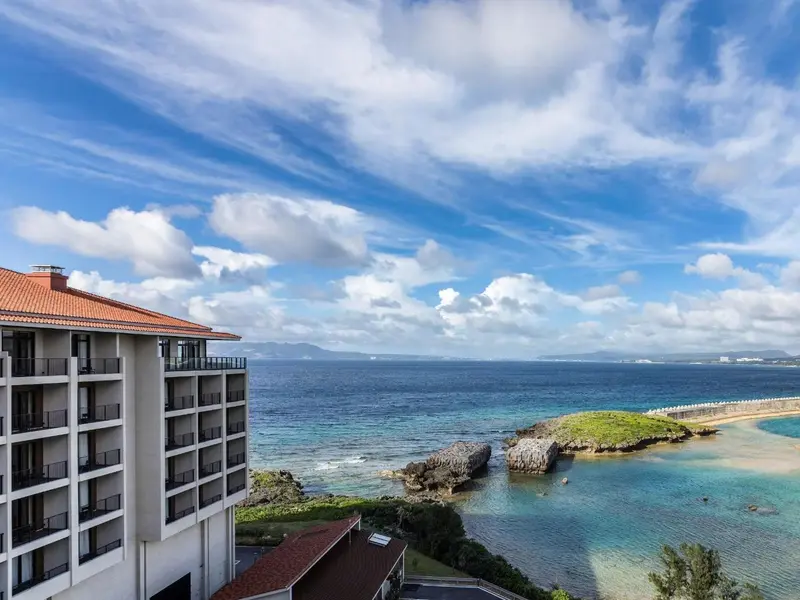 Vue aérienne d'un bâtiment blanc avec un toit en tuiles rouges surplombant la mer et une côte rocheuse.