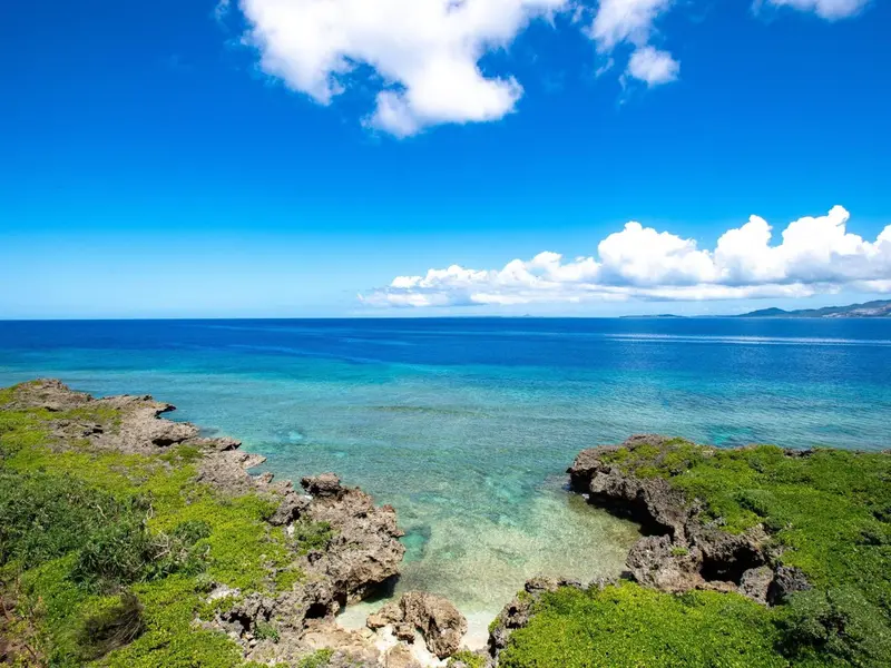 Vue aérienne d'une côte rocheuse avec une eau turquoise et un ciel bleu nuageux.