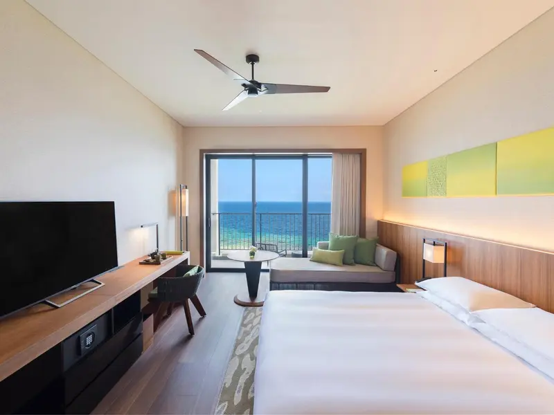 Chambre lumineuse avec vue sur la mer depuis un balcon.