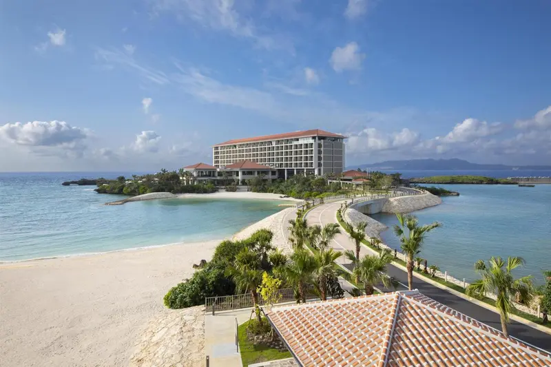 Vue aérienne d'un complexe hôtelier blanc entouré d'une plage de sable clair et d'une eau turquoise.