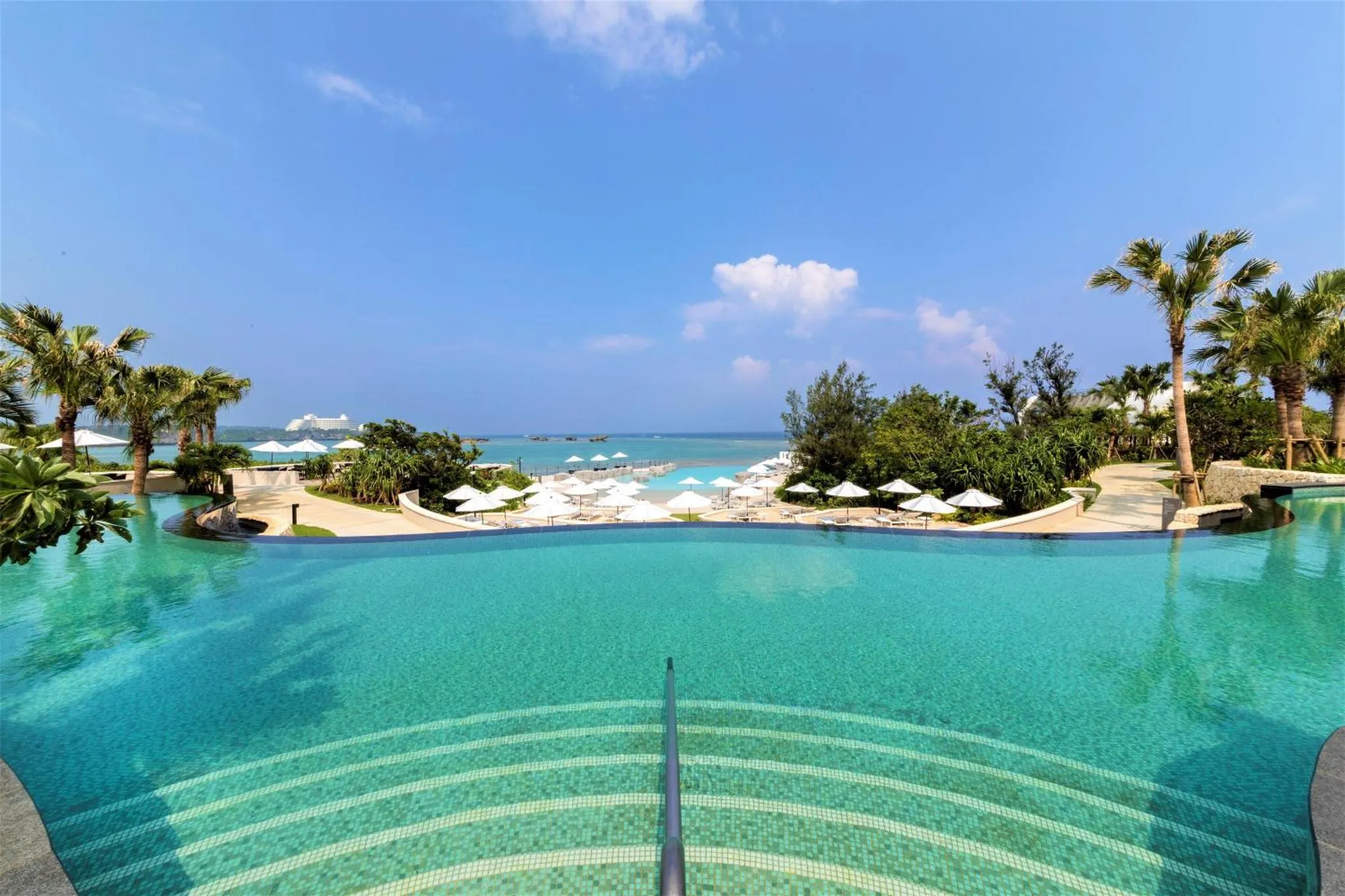 Une piscine à débordement turquoise offre une vue sur la mer et le ciel bleu.