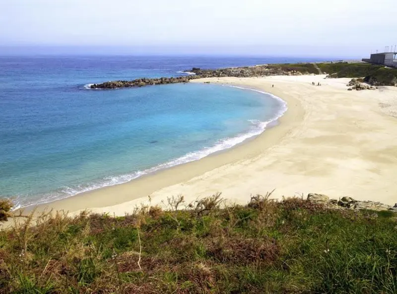 Une plage de sable fin bordée d'une eau turquoise et de rochers.