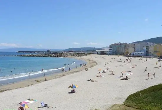Une plage de sable fin bordée par une eau turquoise et des montagnes verdoyantes.