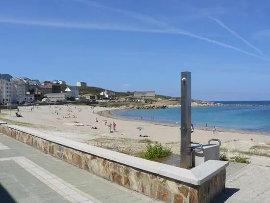 Une plage de sable fin bordée d'une promenade et d'une eau turquoise.