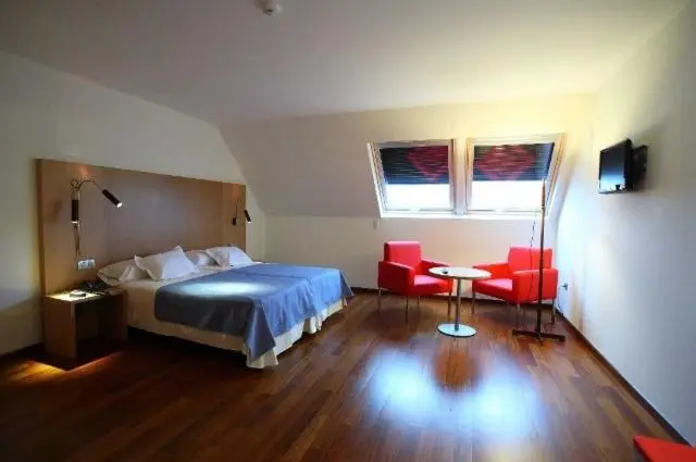 Une chambre lumineuse avec un grand lit et deux fauteuils rouges.