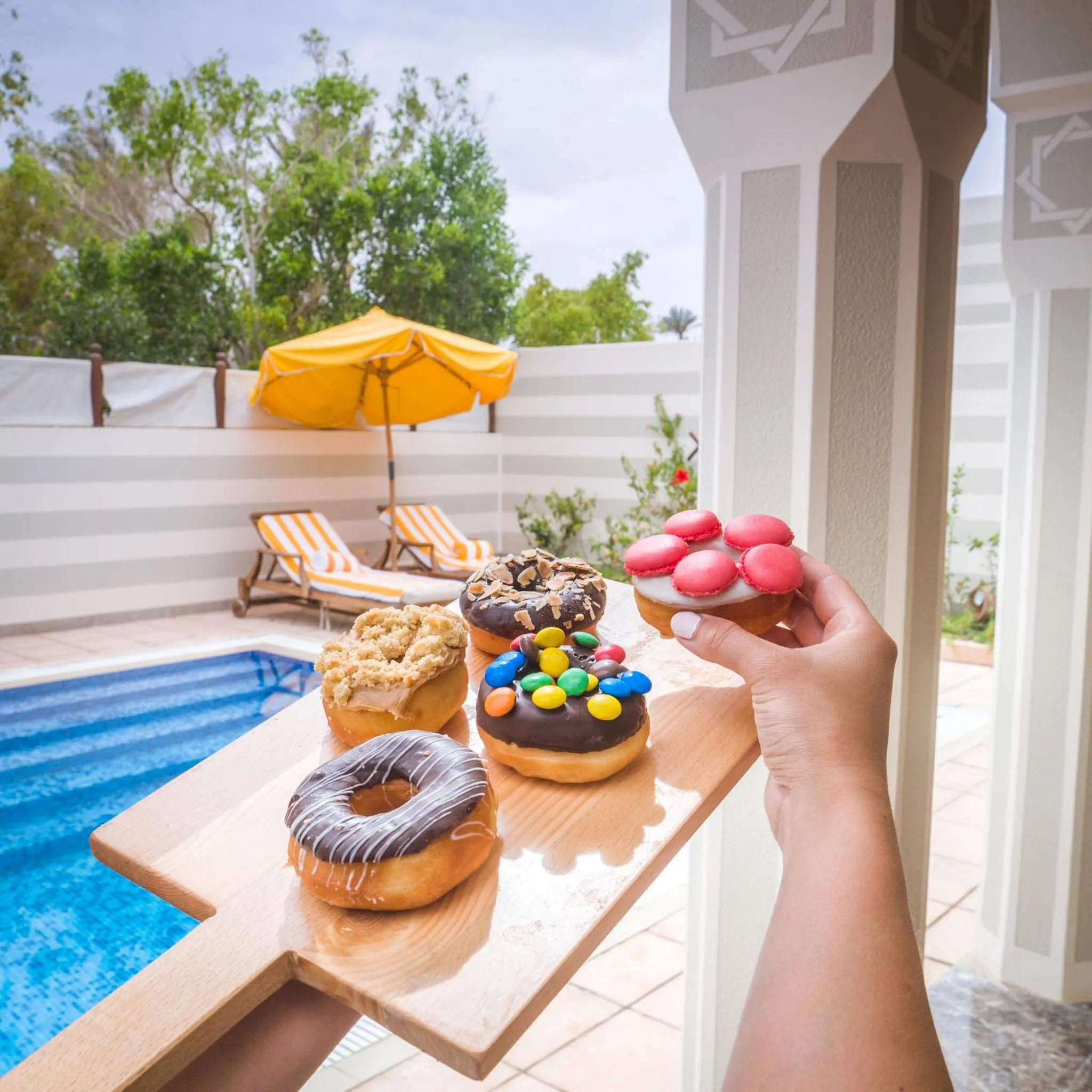 Assortiment de beignets colorés présentés sur une planche en bois au bord d'une piscine.