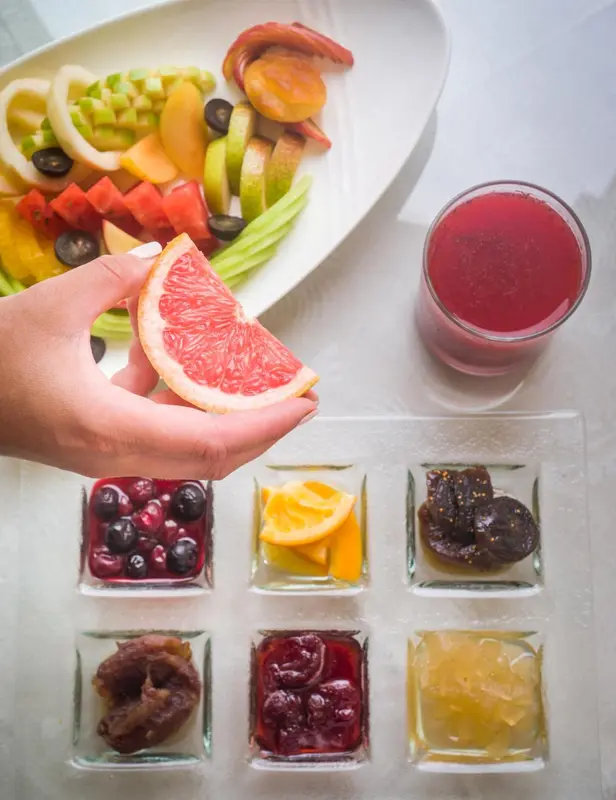 Une main présente une tranche de pamplemousse au-dessus d'une assiette de fruits frais et de jus.