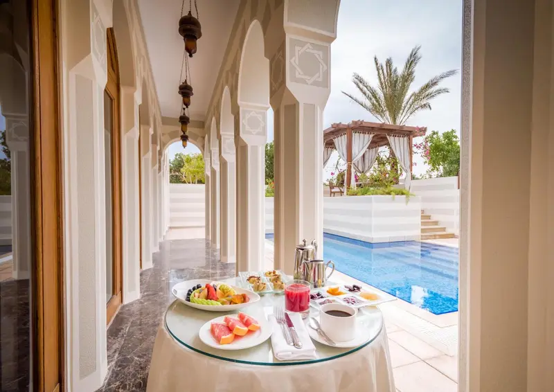 Une table servie pour le petit-déjeuner est placée sur une terrasse avec vue sur une piscine.