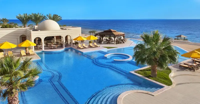 Une piscine bleue bordée de transats et de parasols jaunes, avec une vue sur la mer.