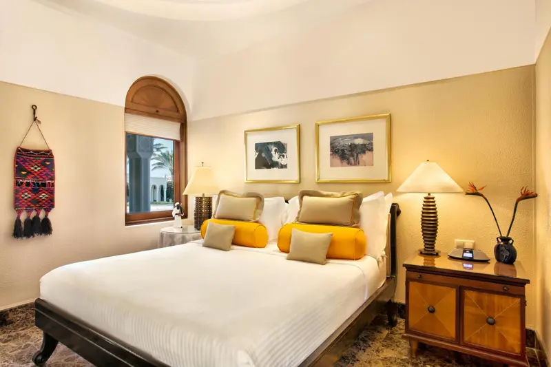 Une chambre lumineuse avec un grand lit recouvert d'une courtepointe blanche et de coussins colorés.