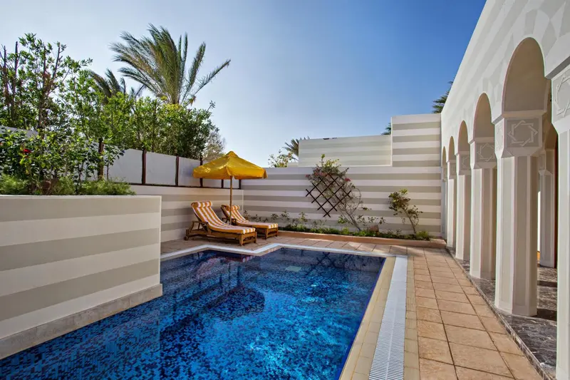 Petite piscine rectangulaire entourée d'une terrasse avec chaises longues et parasols.