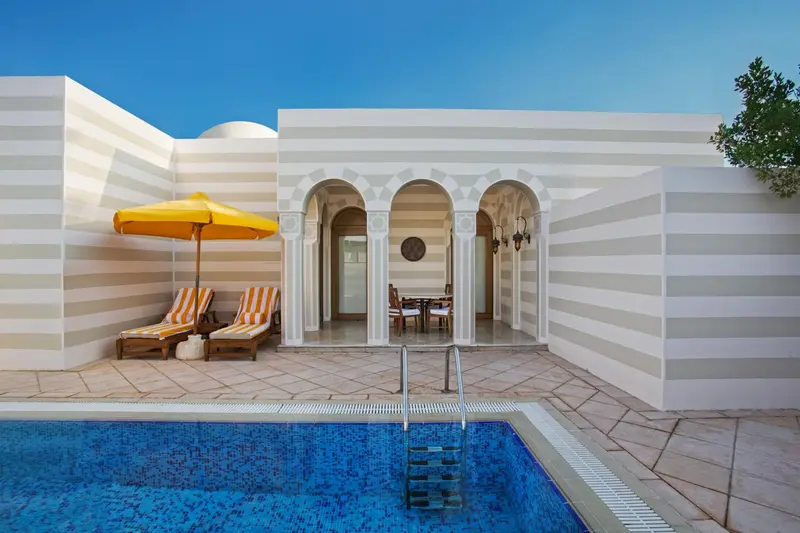 Terrasse avec transats et table à manger près d'une piscine.