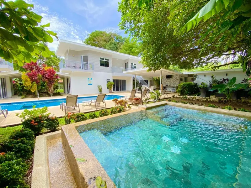 Bâtiment blanc avec piscine et végétation luxuriante.