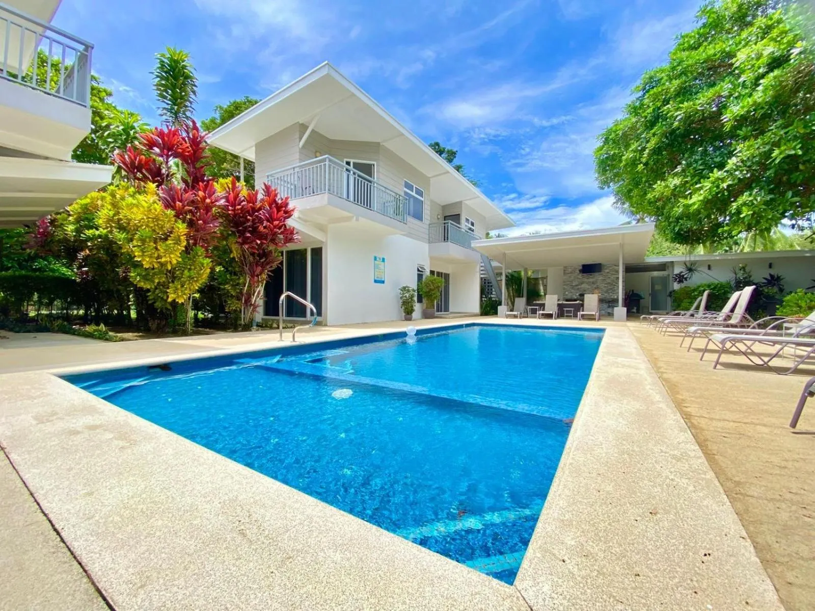 Une piscine rectangulaire turquoise est entourée d'un espace aménagé avec des transats et des palmiers.