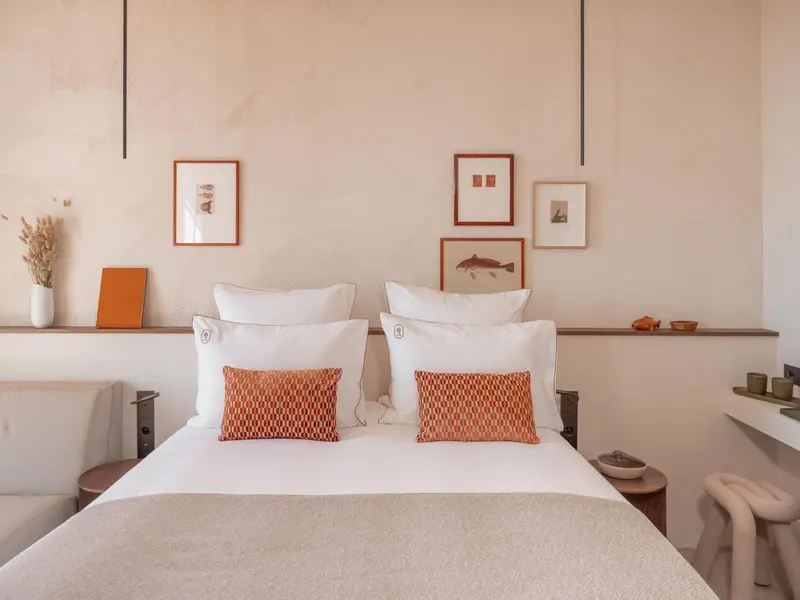 Un lit double avec des oreillers blancs et des coussins orange dans une chambre décorée sobre.